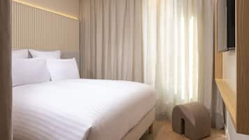 Una habitación de hotel moderna con una cama grande, piso de madera y un televisor fijado a la pared.