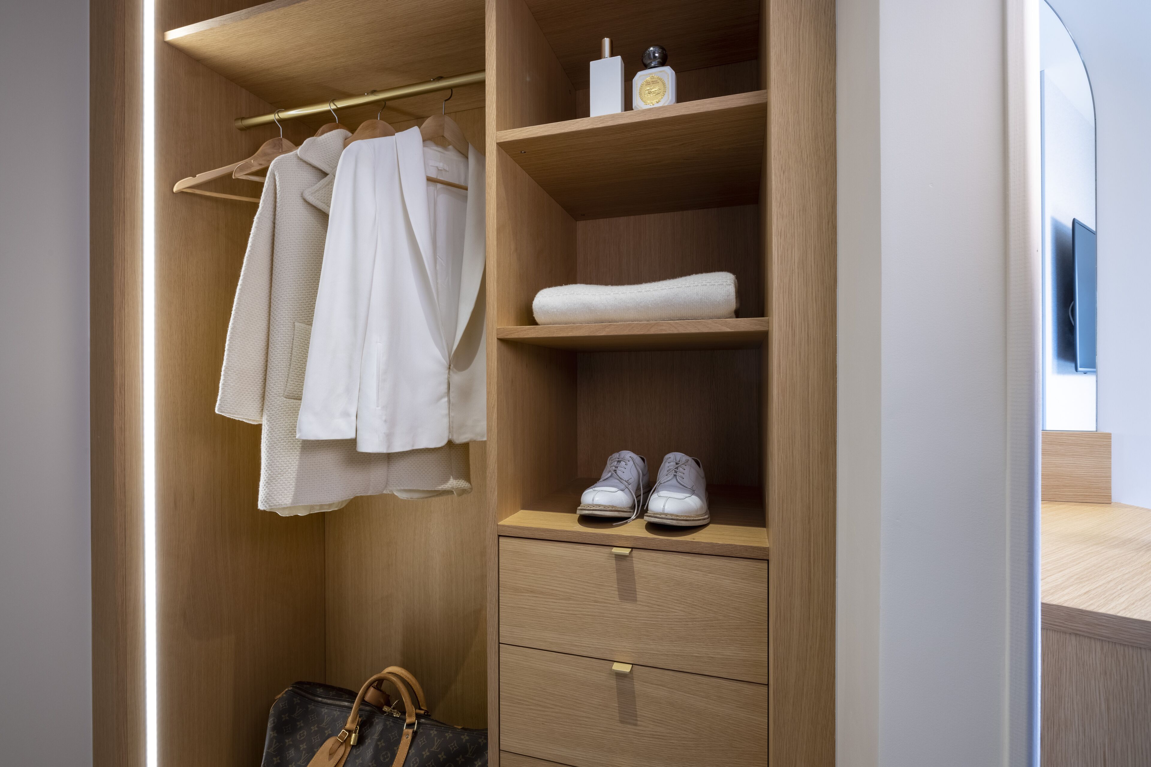 A wooden wardrobe with hanging clothes, a shelf with shoes, and a drawer.