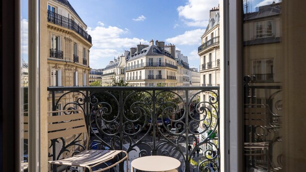 Ein Balkon mit schmiedeeisernen Geländern, einem runden Tisch und einem Streifenstuhl.