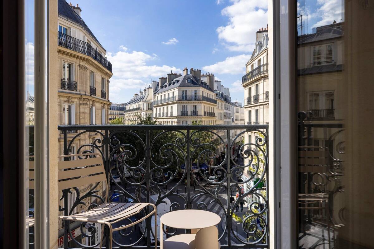Un balcon avec des balustrades en fer forgé, une table ronde et une chaise à rayures.