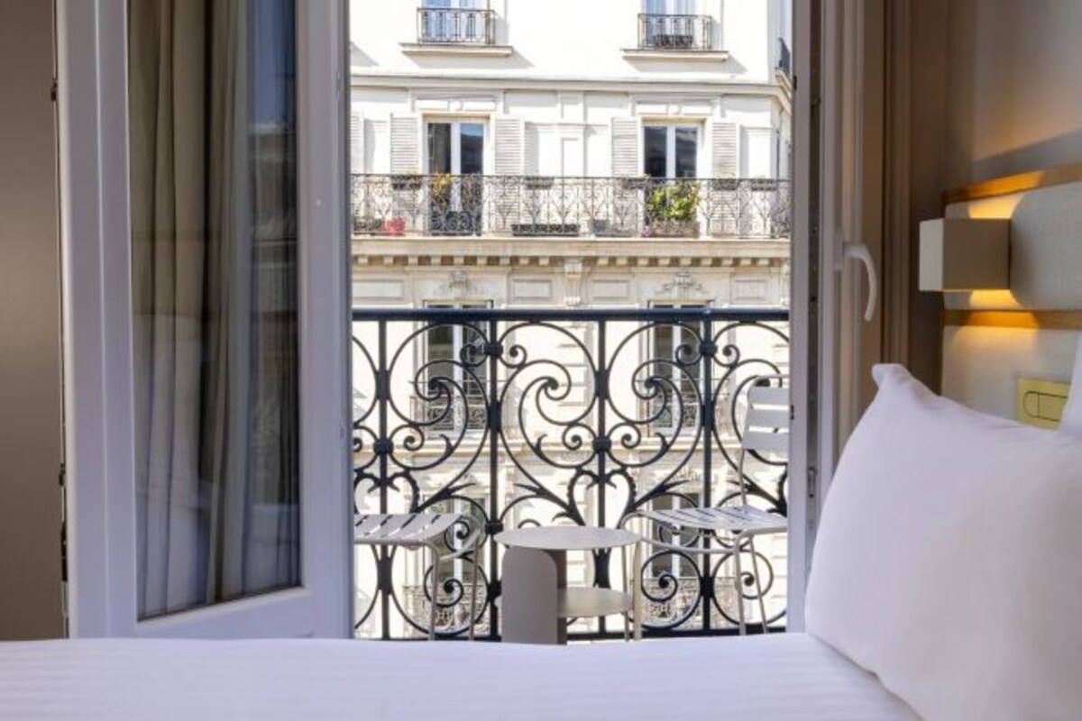 A hotel room with a balcony, a bed, a small table, and a chair.