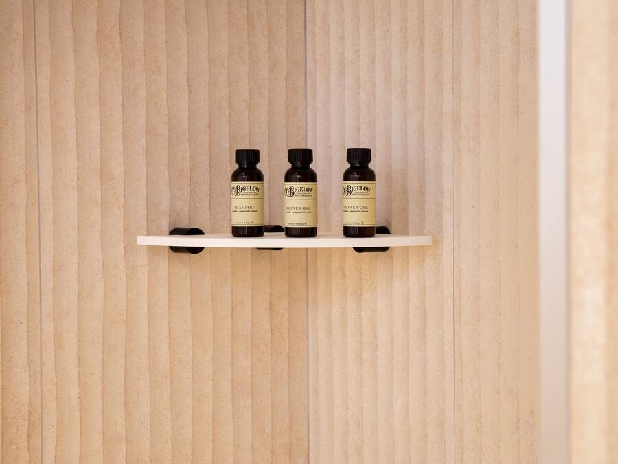 Une étagère avec trois bouteilles de shampoing et de gel douche de la marque Bigelow, le tout adossé à un mur en bois.