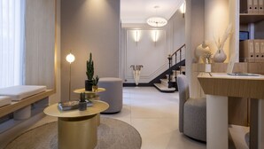 Ein modernes Wohnzimmer mit einem runden, goldenen Tisch, einem grauen Sofa, einem kleinen Tisch mit einer Pflanze und einer Treppe, die zu einer anderen Ebene führt.
