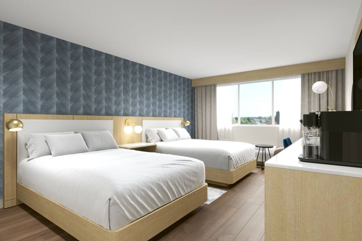 Ein Hotelzimmer mit zwei Betten, einer Küchenzeile und einem großen Fenster mit Blick auf die Stadt.