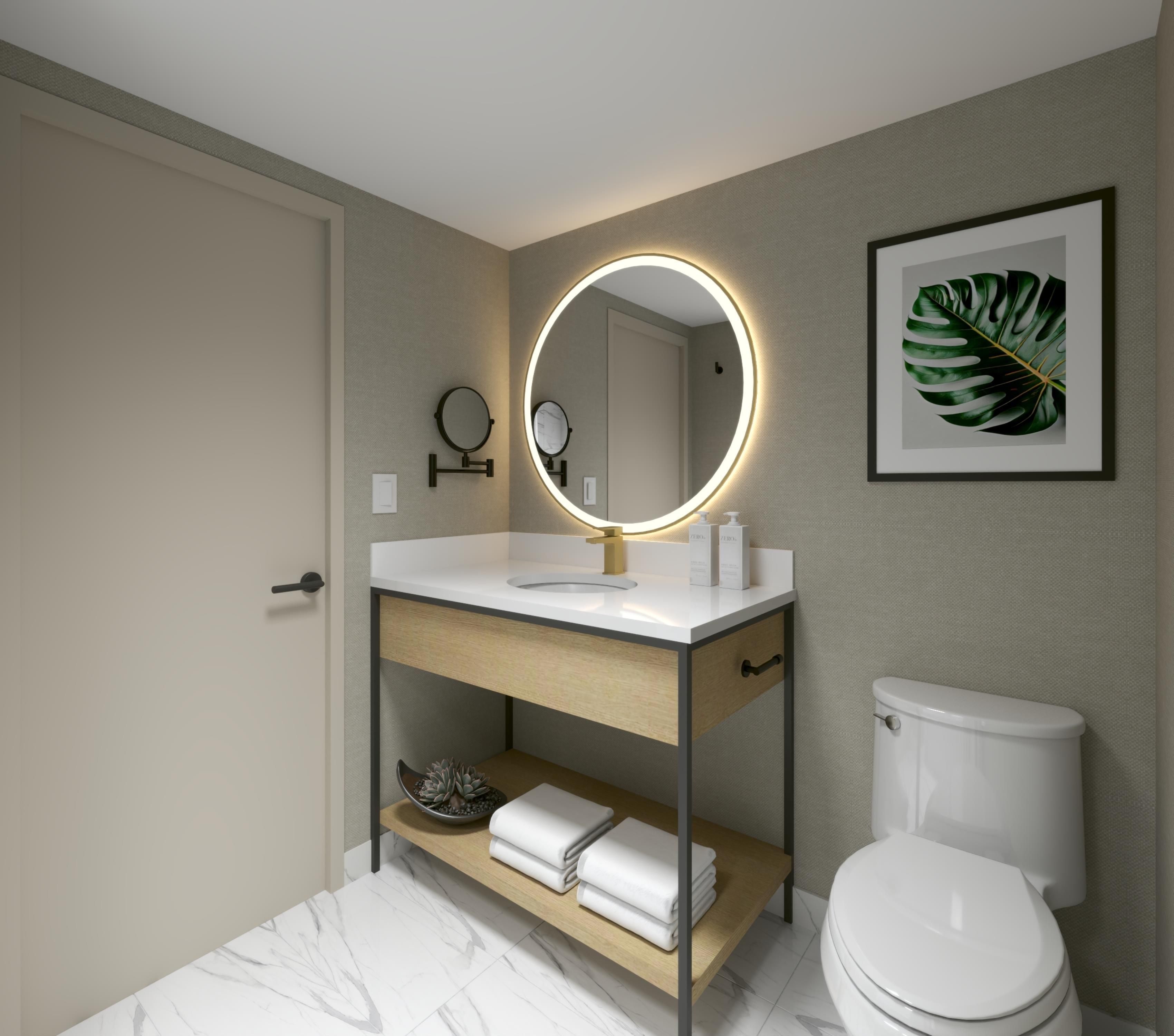 A modern bathroom with a white sink, a round mirror with a light, a toilet, and a framed plant on the wall.