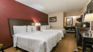 Hotellihuone, jossa on kaksi sänkyä, työpöytä, tuoli, lamppu ja peili.