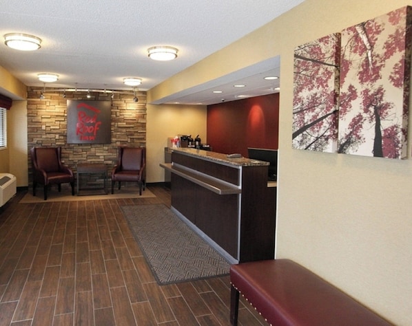 A reception area with a stone wall, a Red Roof sign, a reception desk, and a painting of trees.