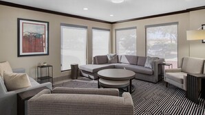 A modern living room with a sectional sofa, a round coffee table, and a patterned rug. There are large windows providing natural light and a view of the outdoors. - Best Western Webster Hotel, Nasa (Webster)