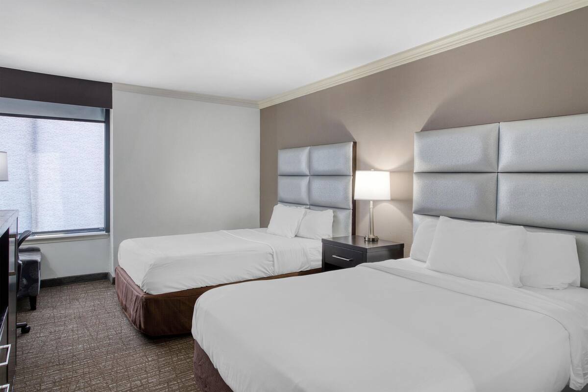 A hotel room with two beds, a desk, and a window.