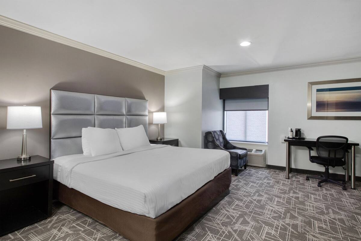 A hotel room with a large bed, a desk, a chair, and a window.