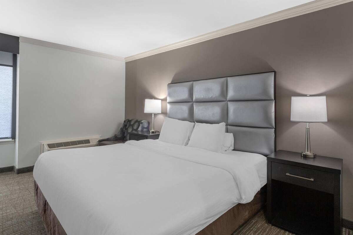 A hotel room with a large bed, two bedside tables with lamps, a headboard, and a window with a view.
