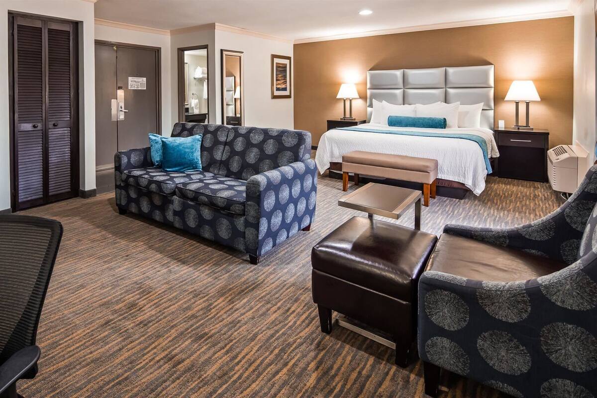 A hotel room with a bed, a sofa, a chair, a small table, and a desk.