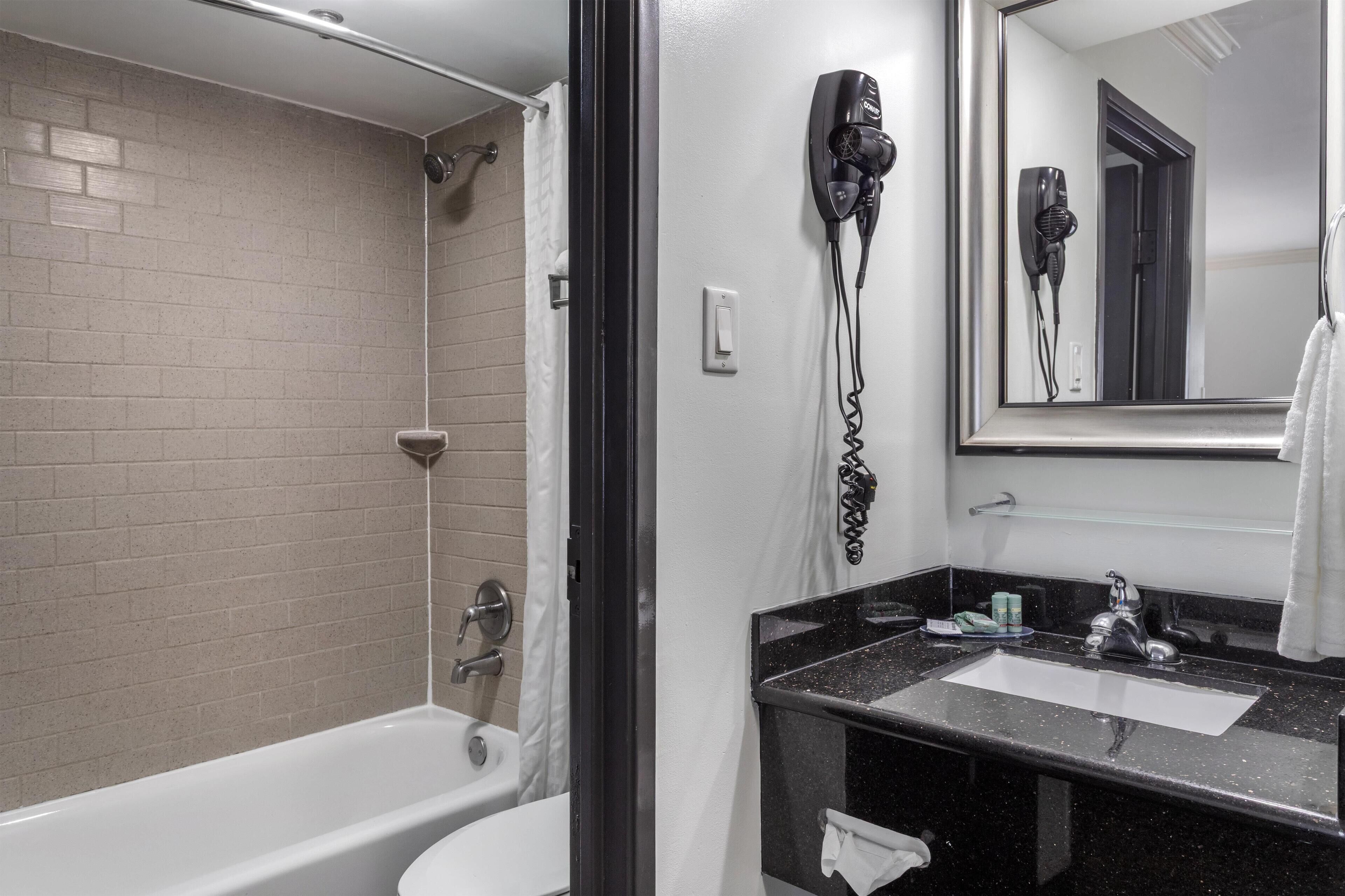 A bathroom with a bathtub, a sink, a hairdryer, and a mirror.