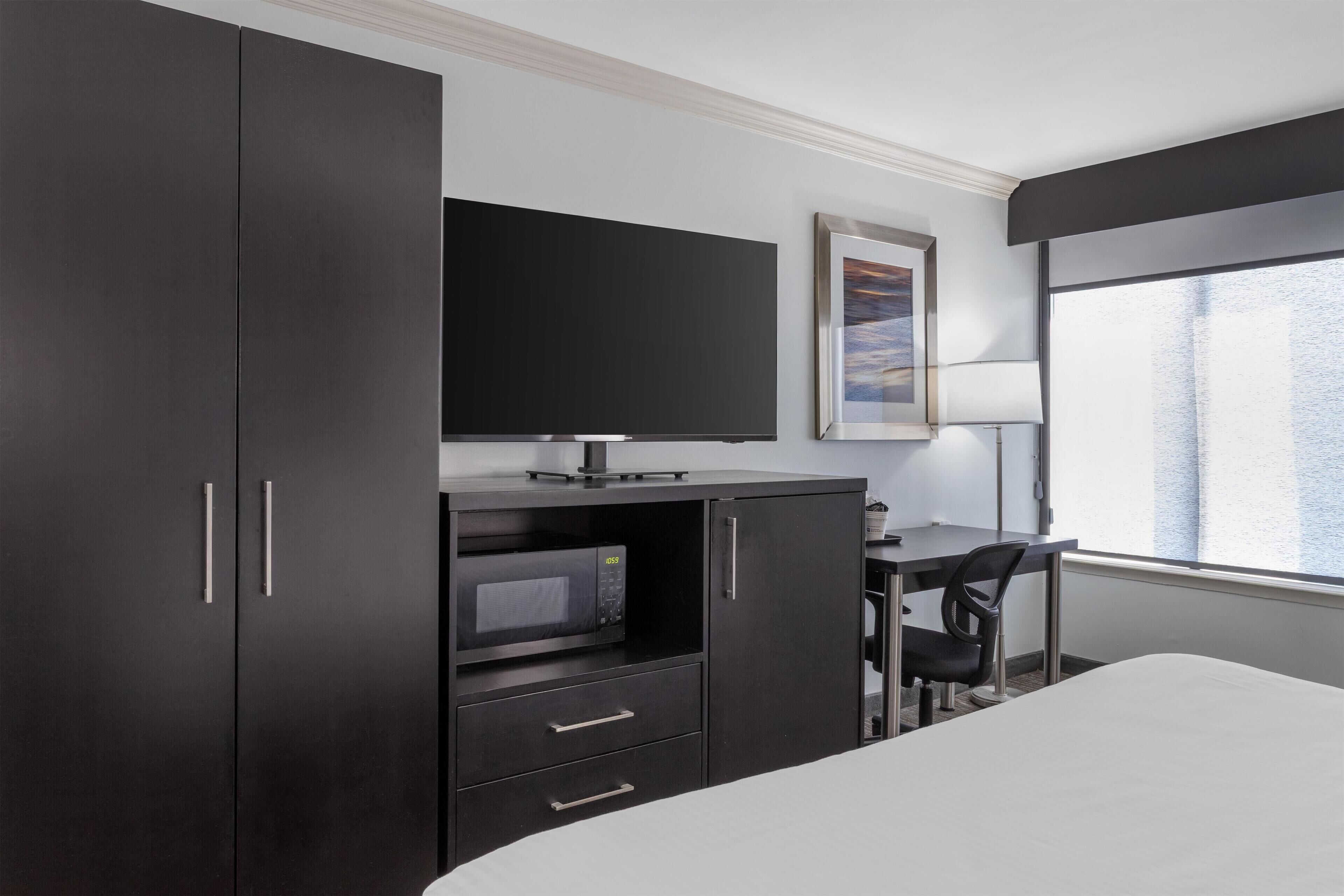 Habitación de hotel con cama, escritorio con silla, televisor, microondas y armario.