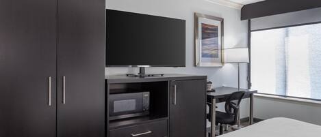 Habitación de hotel con cama, escritorio con silla, televisor, microondas y armario.