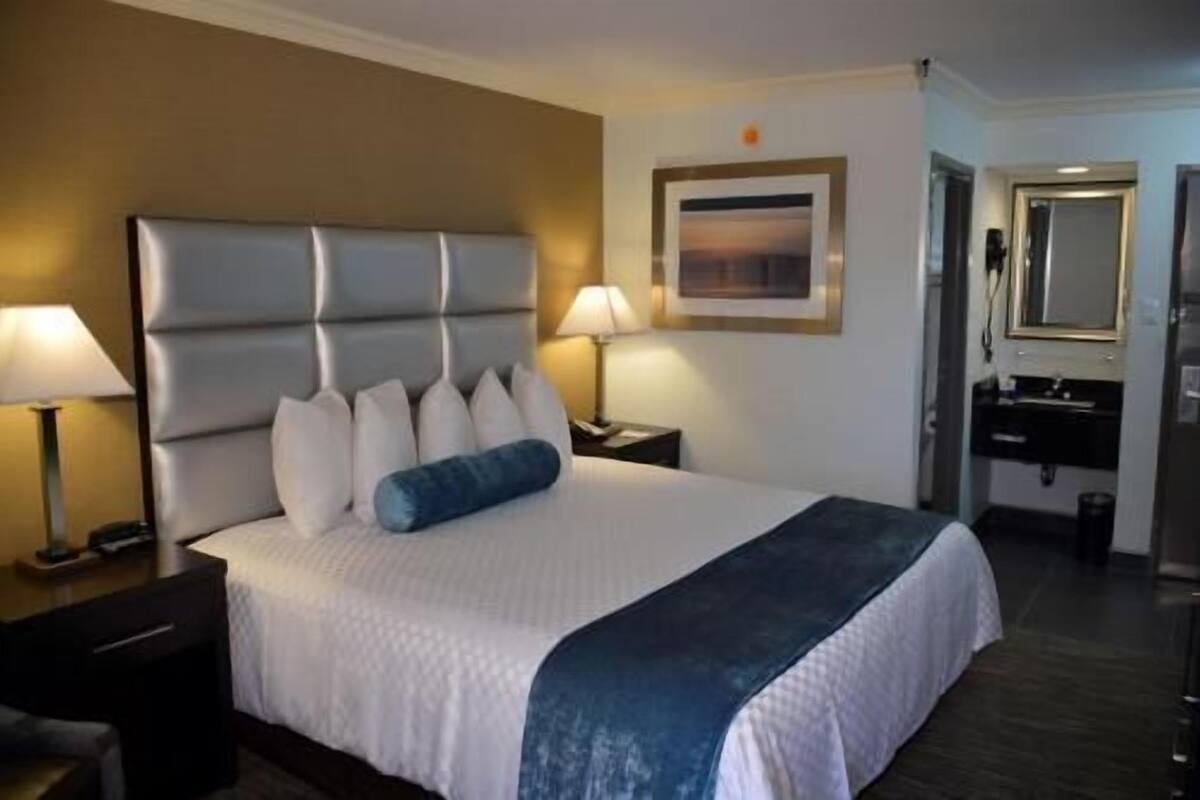 A hotel room with a large bed, two bedside lamps, a nightstand, a dresser, and a mirror.