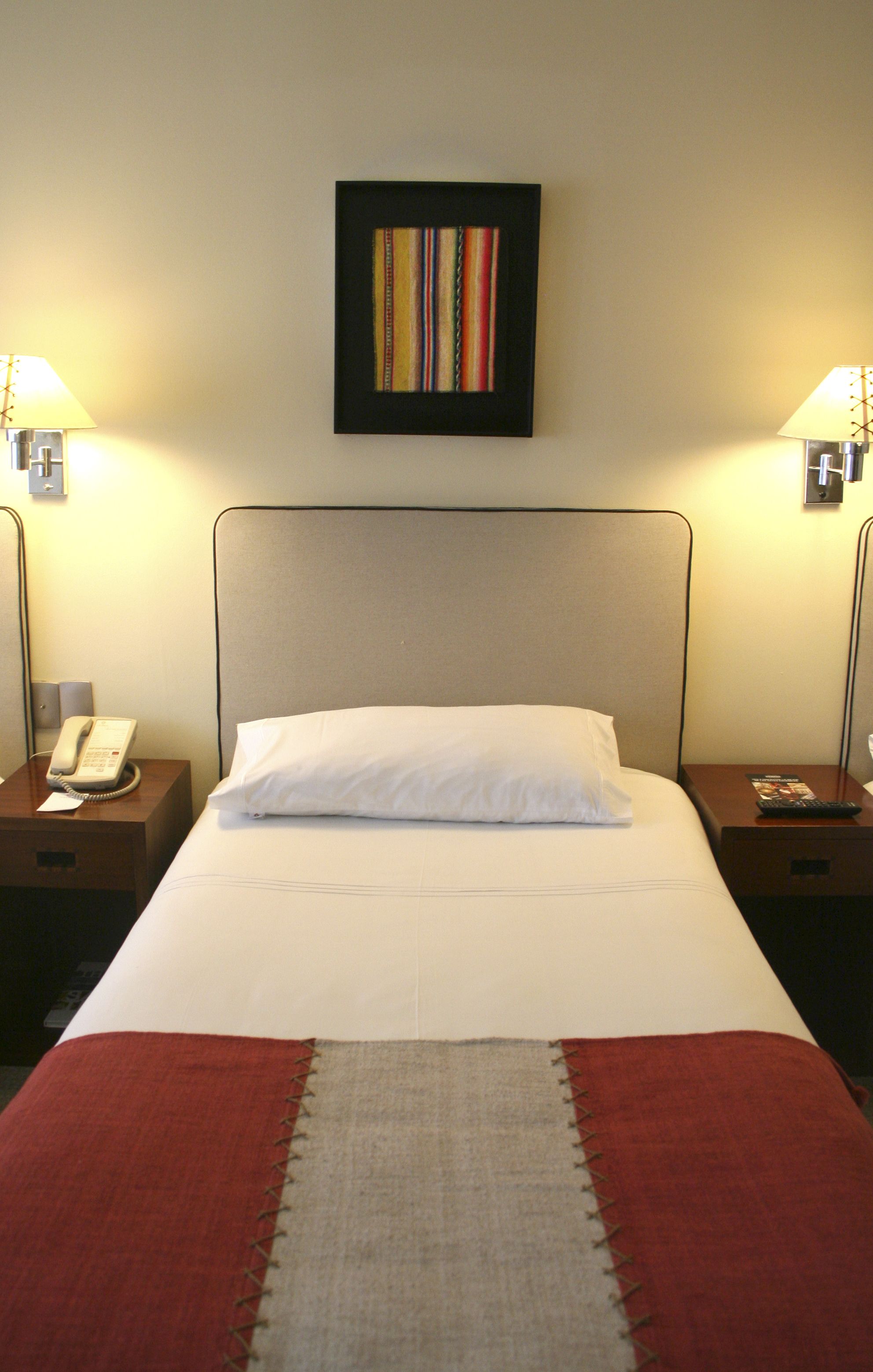 Ein Hotelzimmer mit einem Bett, einem Telefon, zwei Lampen und einem gerahmten Bild an der Wand.