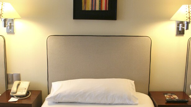 Een hotelkamer met een bed, een telefoon, twee lampen en een lijst met een afbeelding aan de muur.