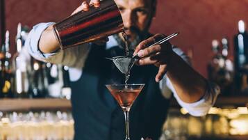 Un barman vertiendo una bebida en una copa de martini usando un colador.