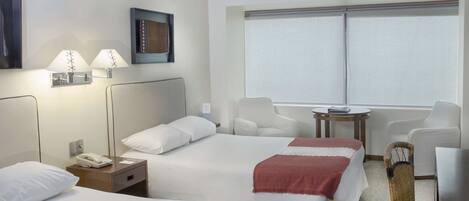 Habitación de hotel con dos camas, un escritorio, una silla y una ventana con persianas.