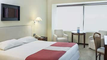 A hotel room with a bed, a desk, two chairs, a lamp, and a window.