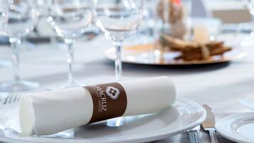 Een net gedekte eettafel met een opgerolde servet, een bord met een belegd broodje en een glas water.