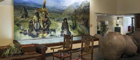A lobby with a large mural, wooden chairs, a sofa, and large vases.