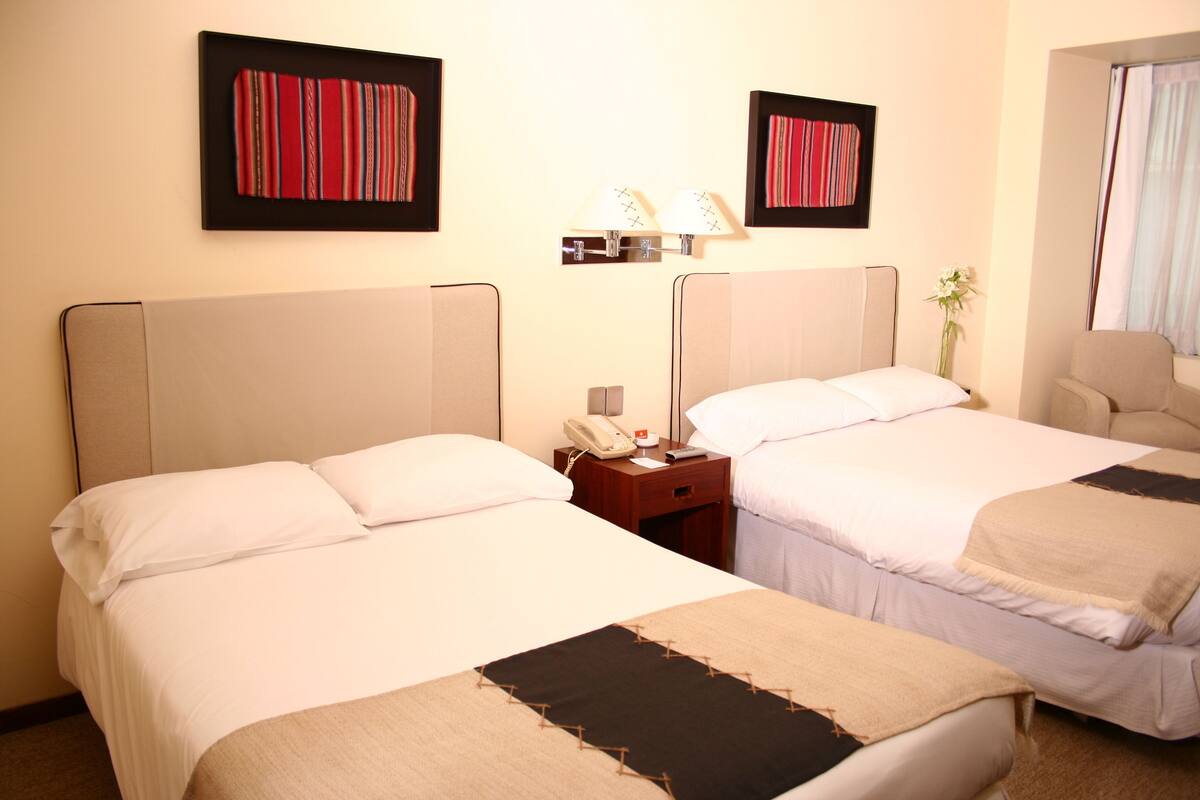 Une chambre d’hôtel avec deux lits, une table de chevet avec un téléphone et des lampes fixées au mur.