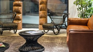 Un espace de détente moderne avec un canapé en cuir, des fauteuils en osier, une table basse ronde et de hauts piliers en bois.