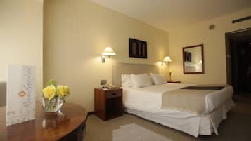 A hotel room with a bed, bedside tables, lamps, a vase with flowers, and a sign on the wall.