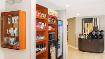 A kitchenette with a refrigerator, microwave, and various food items.