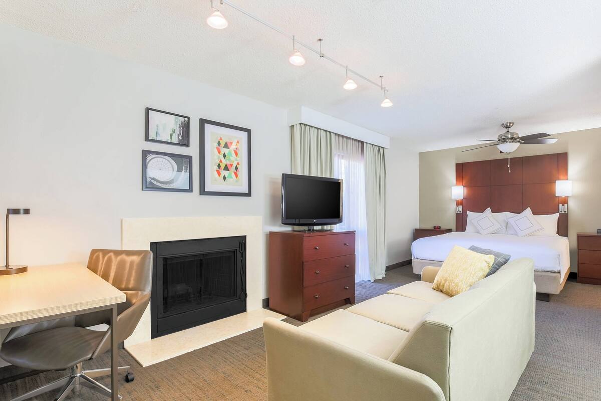 A hotel room with a bed, a TV, a fireplace, a sofa, and a desk.