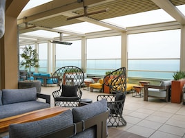 A spacious outdoor seating area with a view of the ocean, featuring modern furniture and a pergola structure.