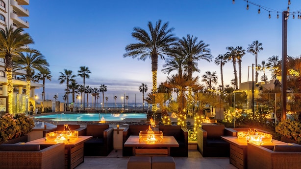 A rooftop bar with outdoor seating, a pool, and palm trees. - The Waterfront Beach Resort, A Hilton Hotel (Huntington Beach)