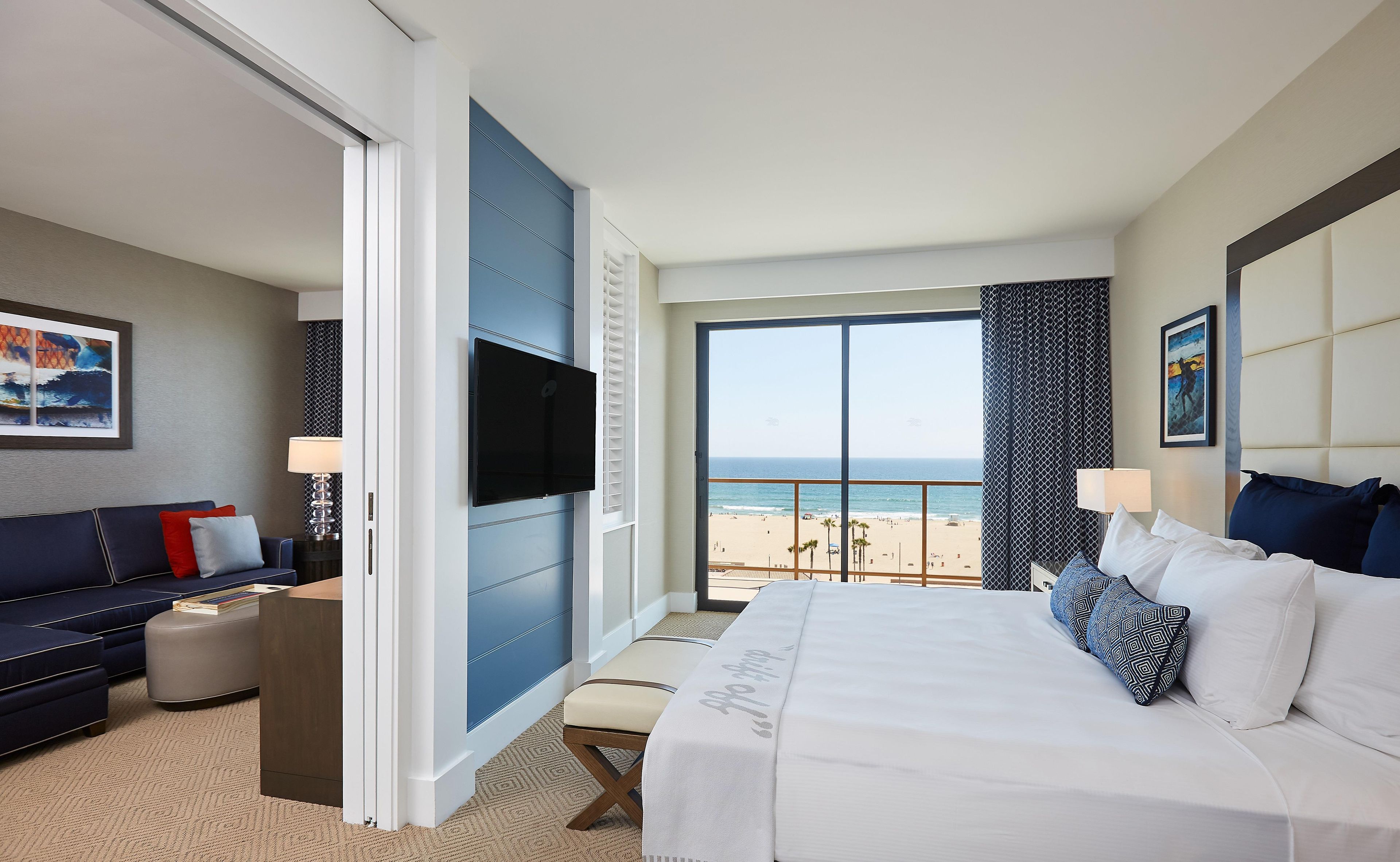 Une chambre d’hôtel avec un lit, un canapé, une télévision et vue sur la plage.