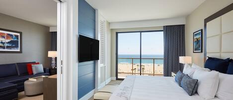 A hotel room with a bed, a sofa, a TV, and a view of the beach.