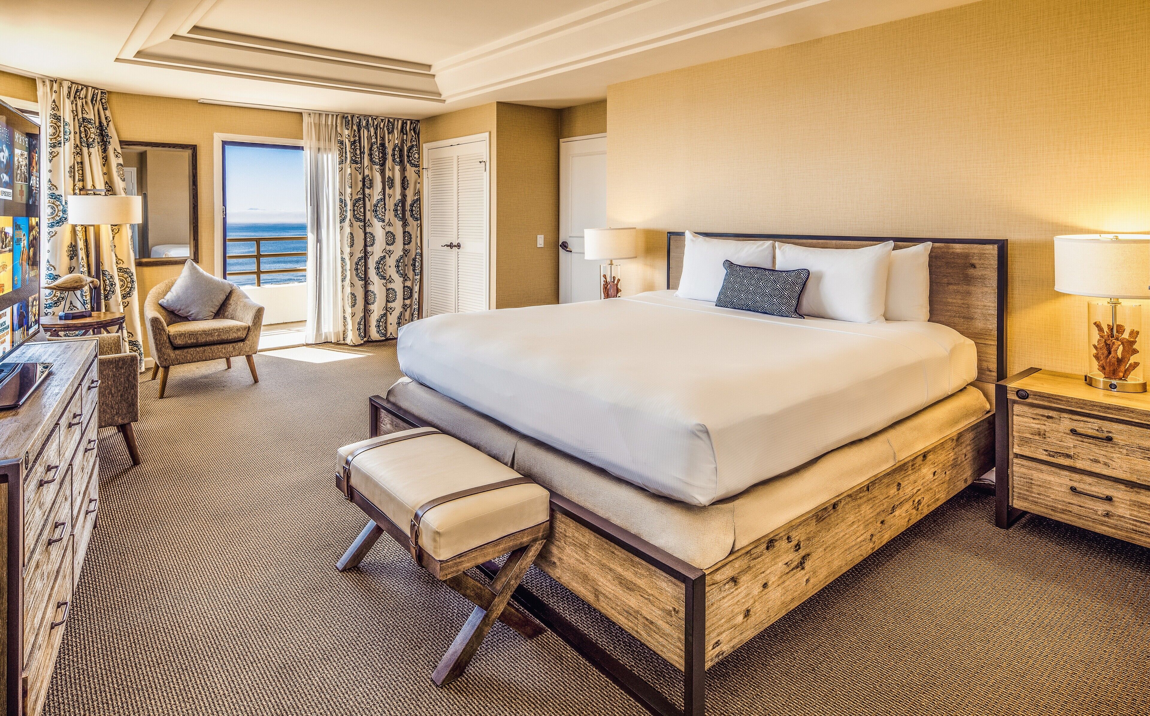 A spacious hotel room with a large bed, a desk with a chair, a small seating area, and a view of the ocean.