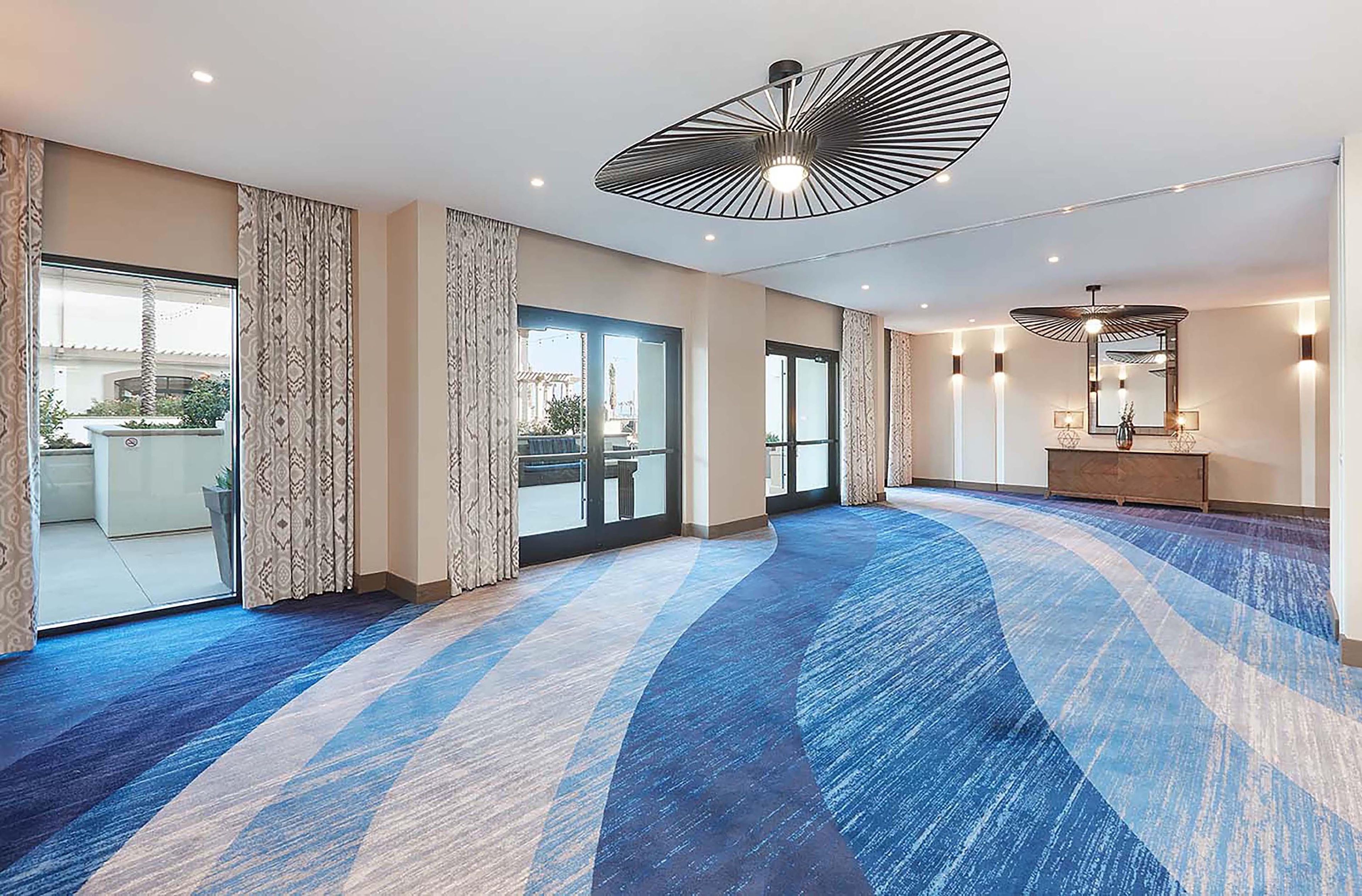 Un hall d’hôtel doté d’un tapis à motifs, de grandes fenêtres et d’un luminaire moderne au plafond.