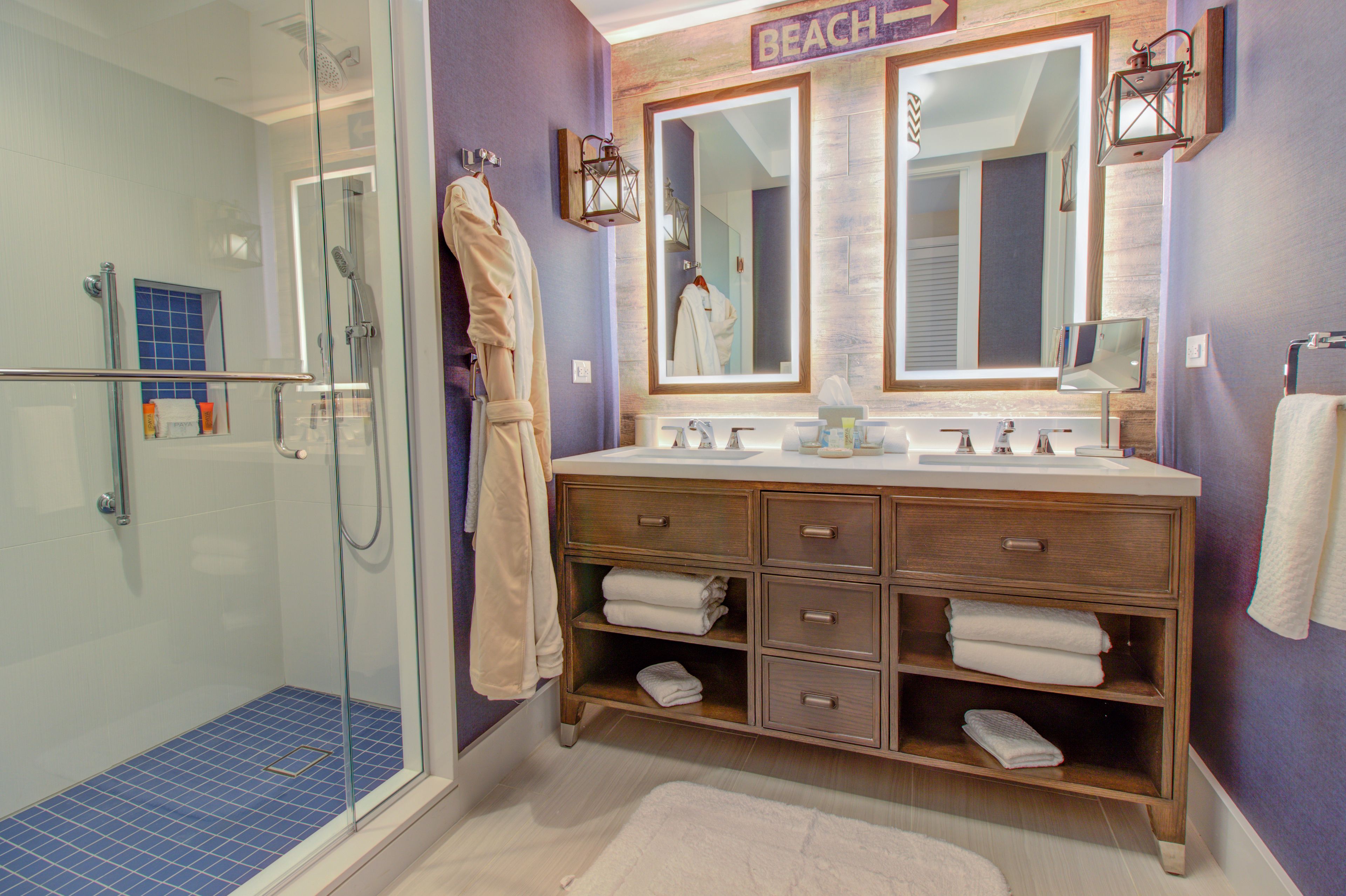 A bathroom with a glass-enclosed shower, a vanity with a mirror, and a sign that reads "BEACH".