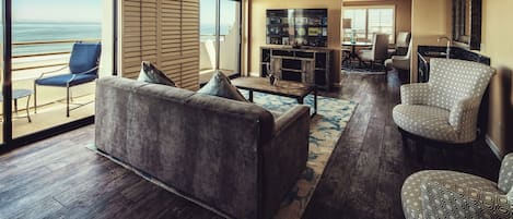 A spacious living area with a large flat-screen TV, comfortable seating, and a view of the ocean through large sliding doors.