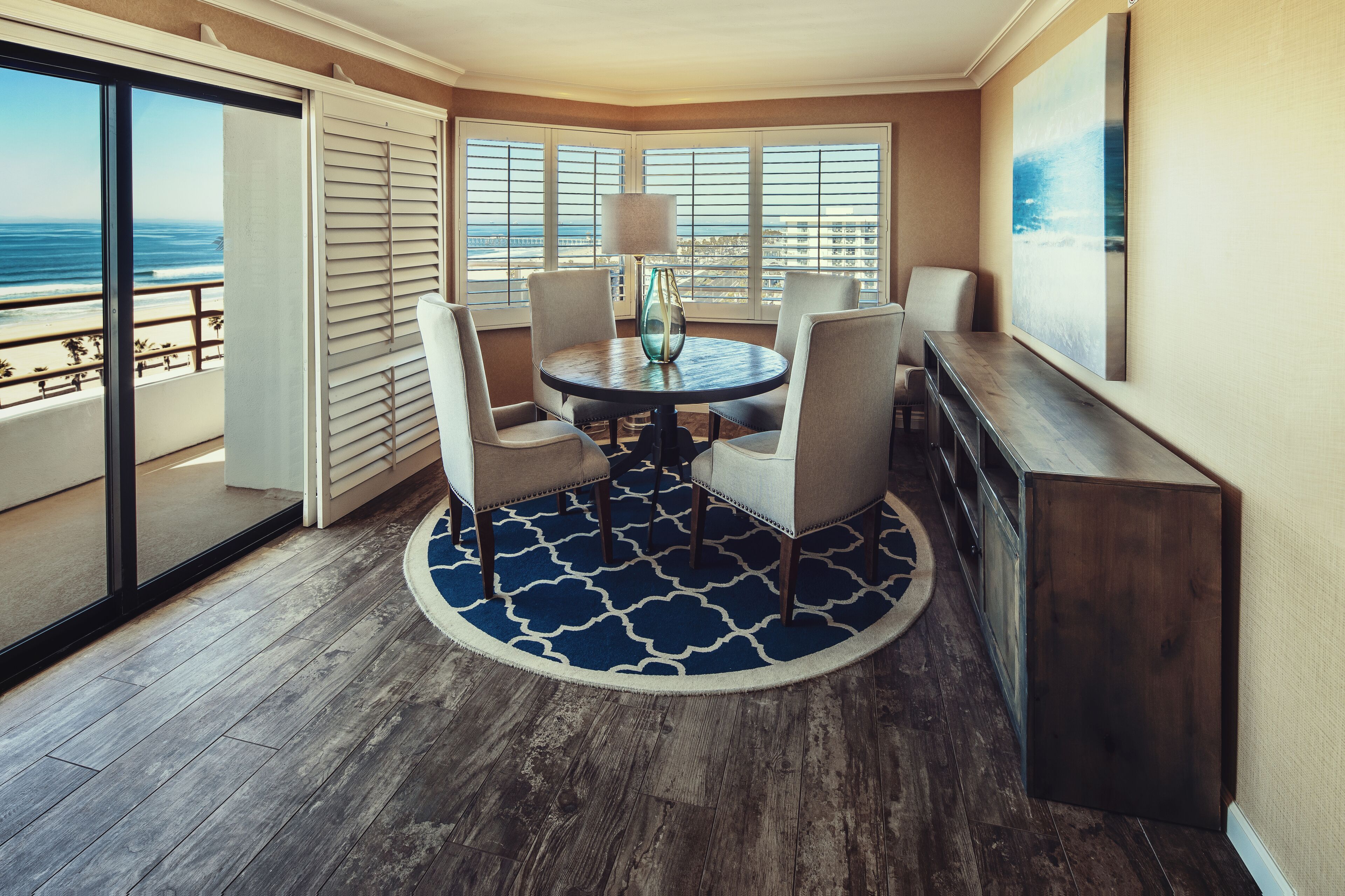 A corner room with a round table, four chairs, a lamp, and a view of the ocean.