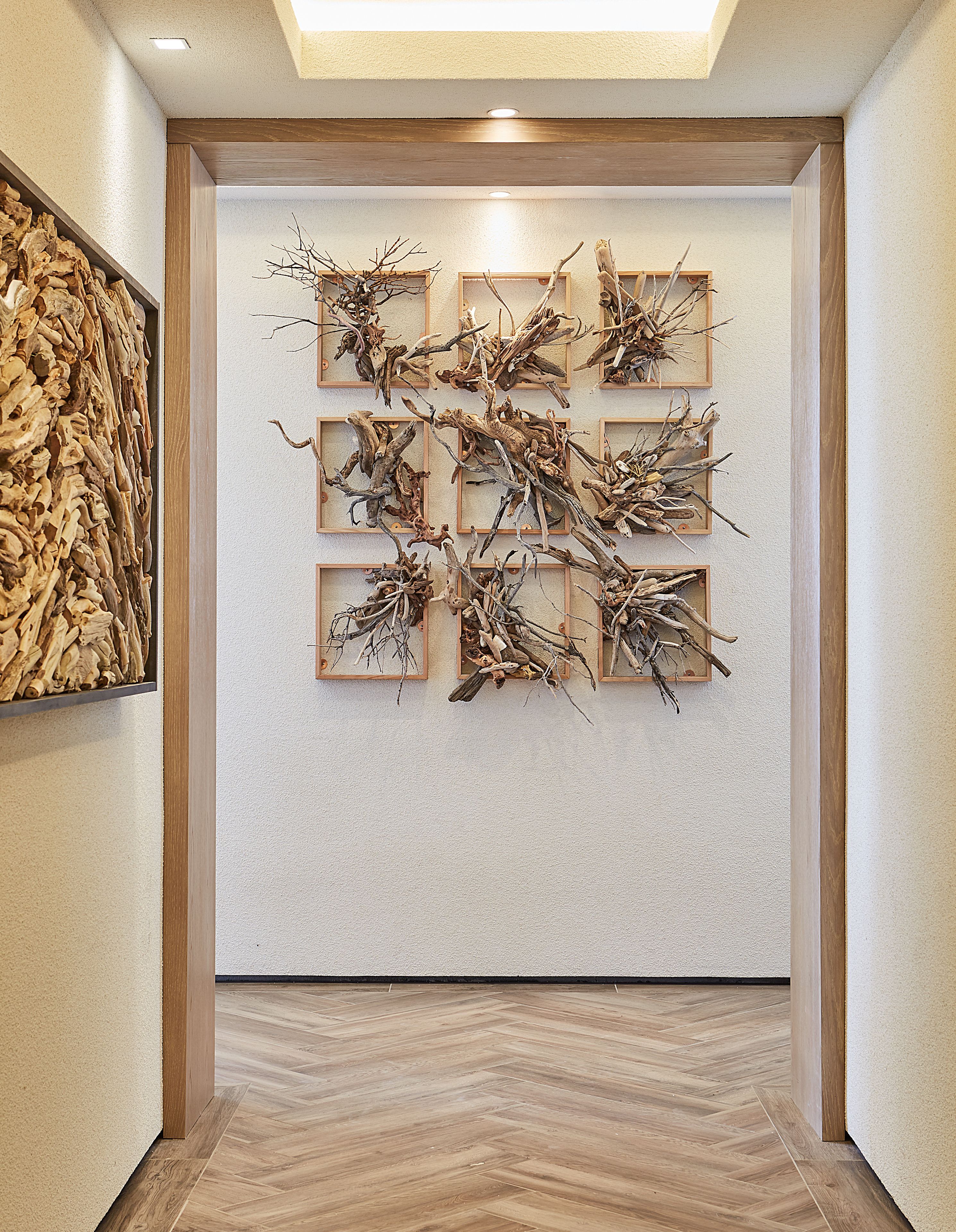 A hallway with a wooden floor, a wall-mounted abstract art piece, and a framed picture on the left.