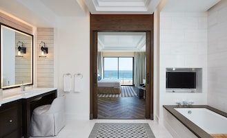 A modern hotel bathroom with a large bathtub, a vanity with a mirror, and a television.