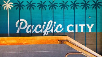 Ein Holzschild mit der Aufschrift 'Pacific City', zeigt stilisierte Palmen.