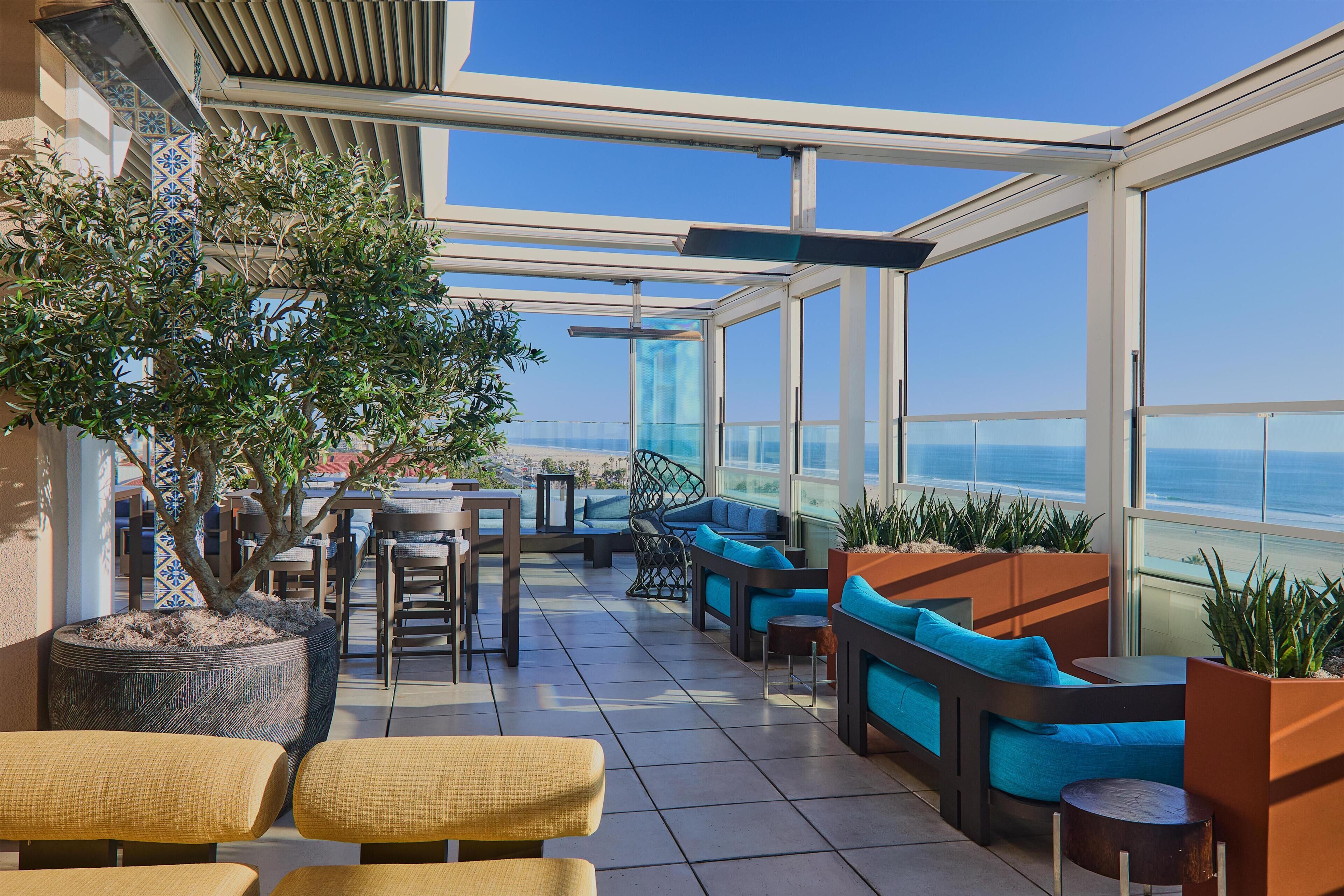 A rooftop terrace with seating, a potted tree, and a view of the ocean.