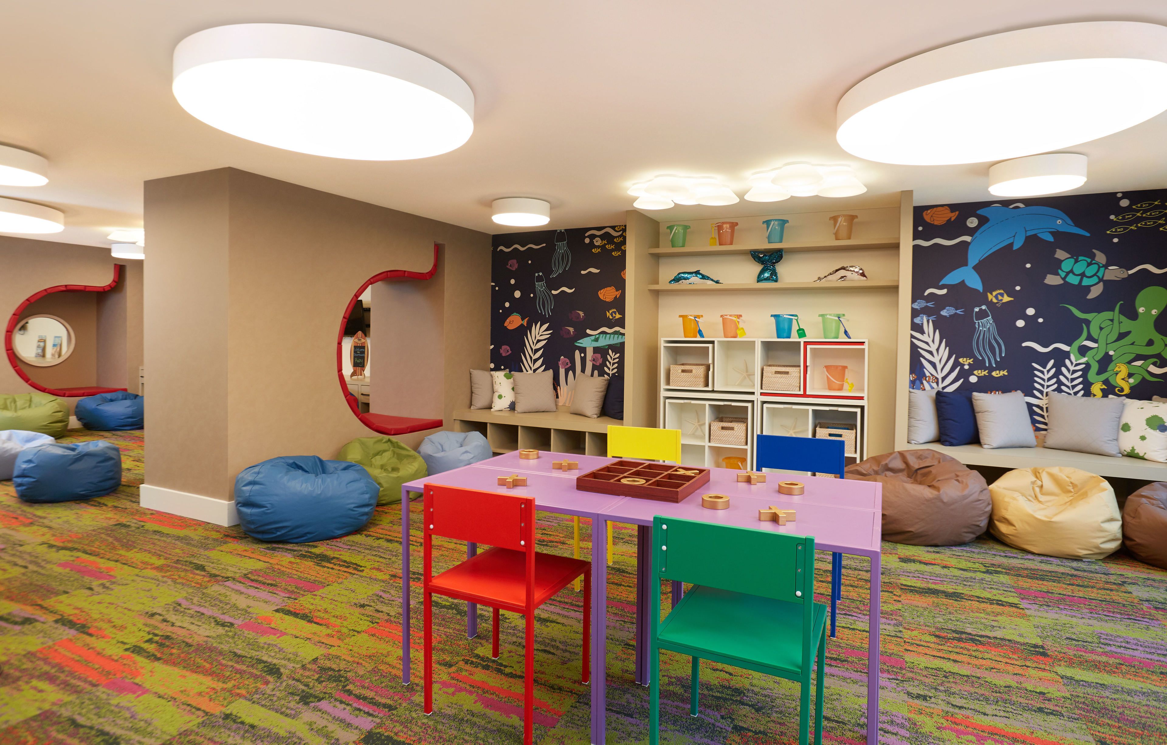 A children's playroom with colorful furniture, a table with toys, and shelves with storage bins.