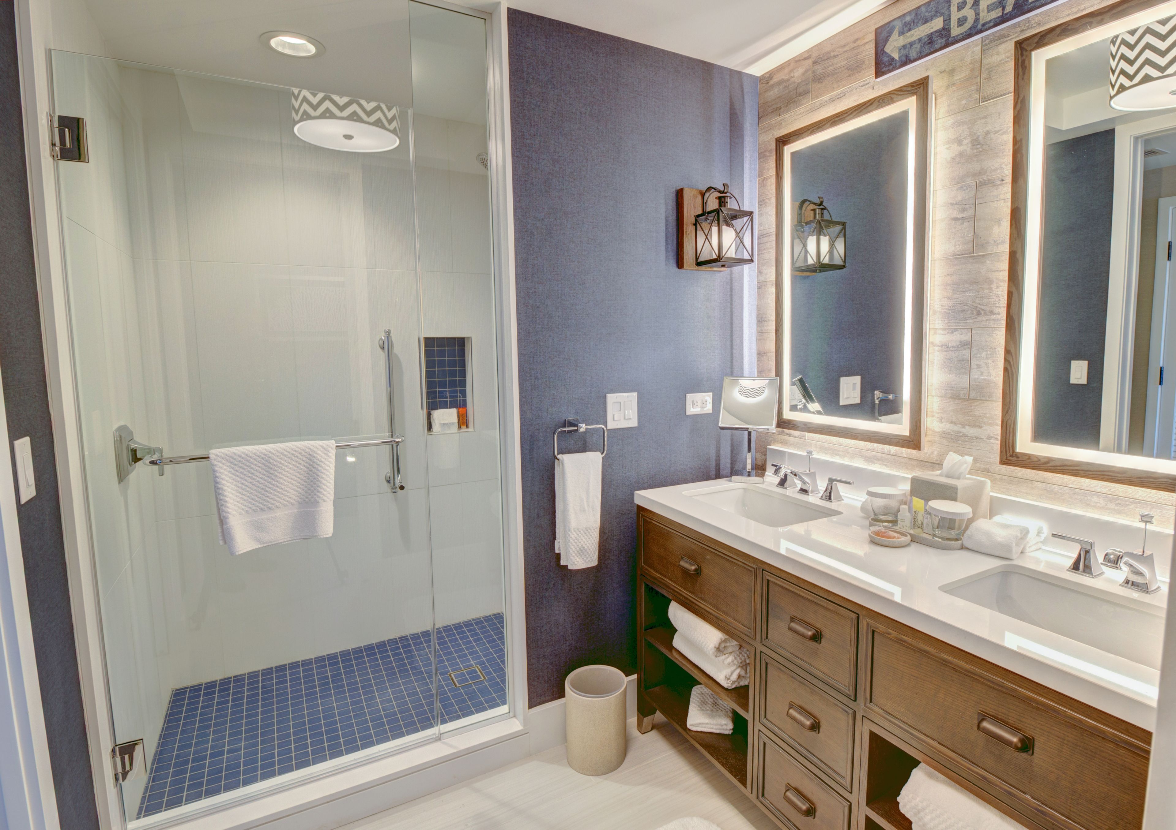 A modern bathroom with a glass shower enclosure, a vanity with a large mirror, and a blue-tiled shower floor.