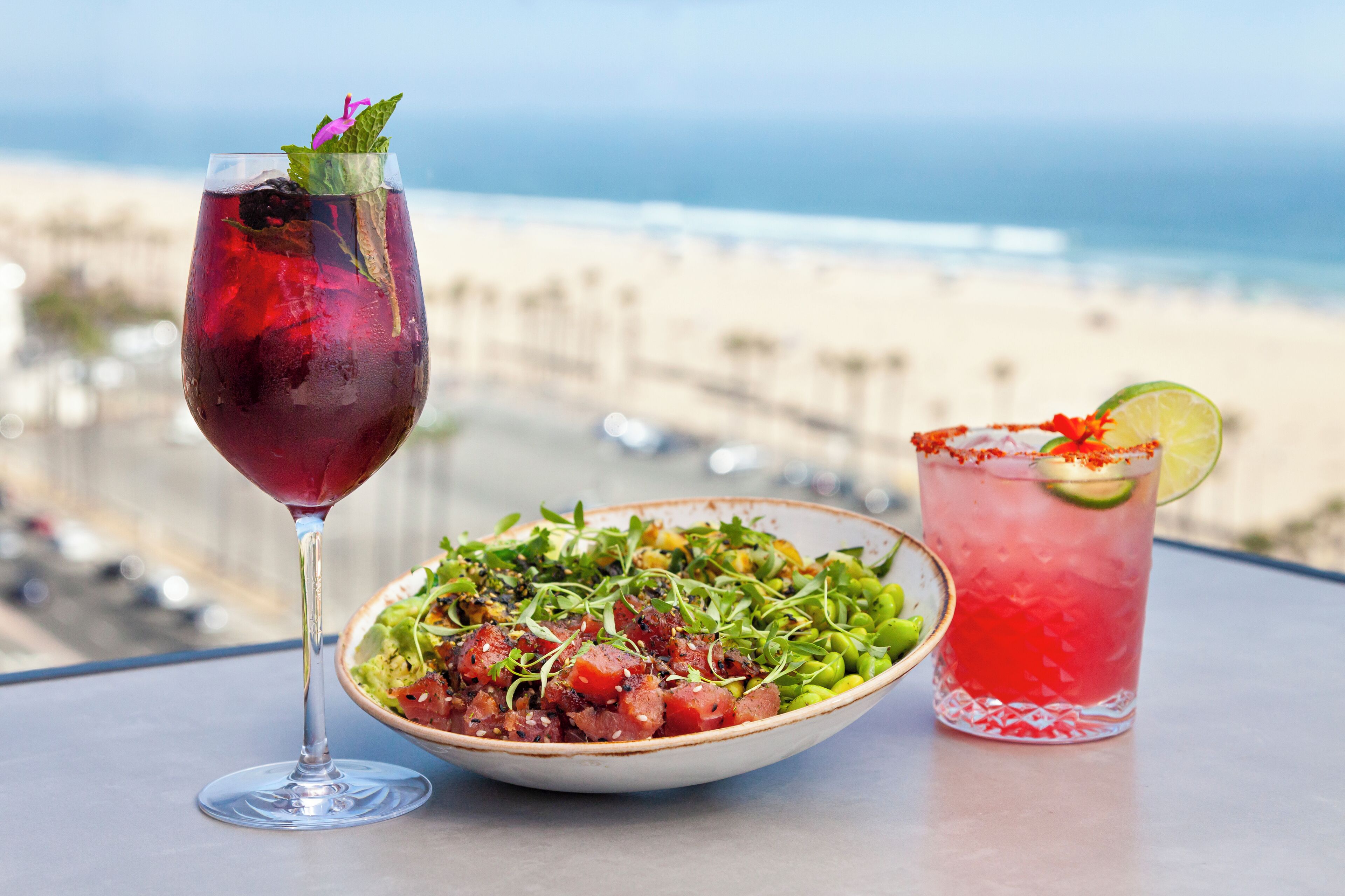 Ein Tisch mit einem Glas rotem Cocktail, einer Salat-Schüssel und Blick auf den Strand.
