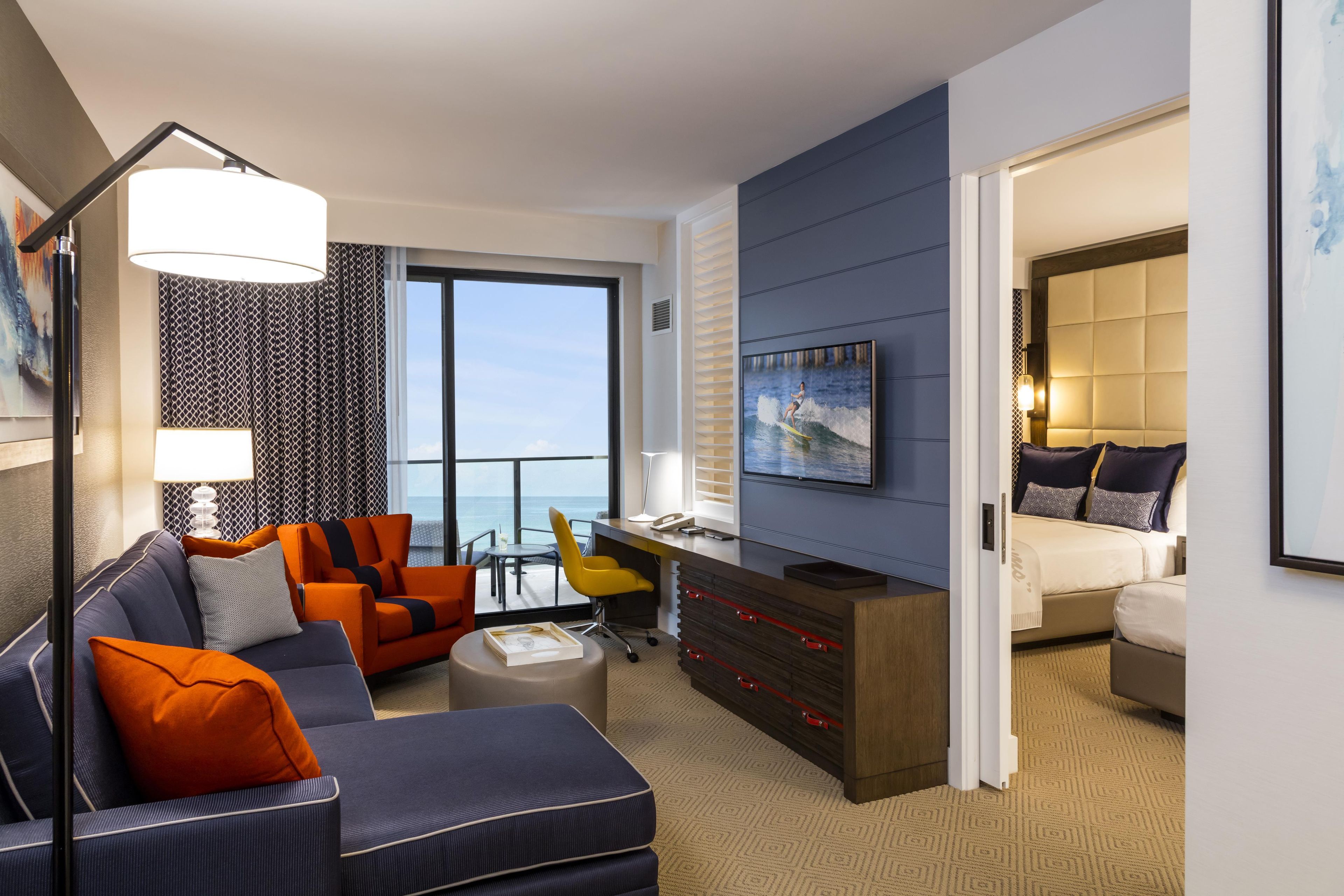 A modern hotel room with a balcony, a sofa, a desk, and a bed.