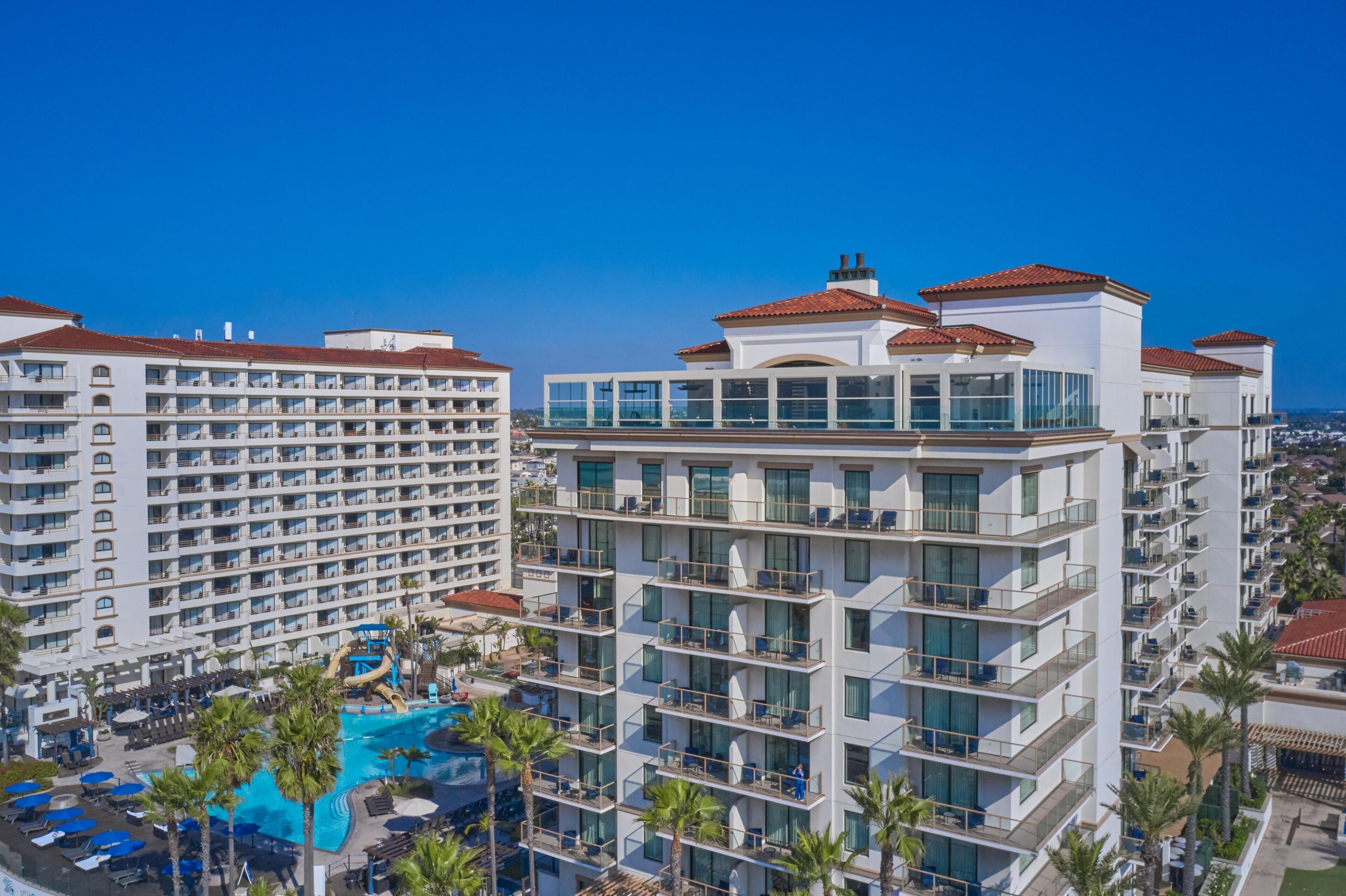 A multi-story hotel with balconies, a swimming pool, and a clear blue sky.